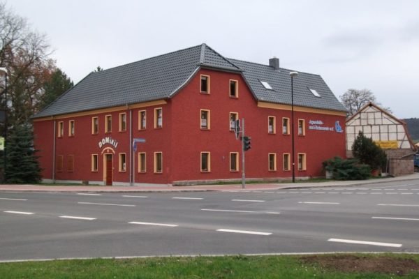 rotes Gebäude hinter einer Straßenkreuzung, Eingangsschild:Domizil.