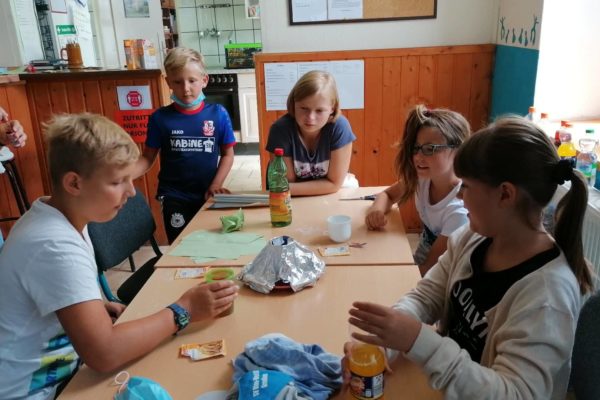 Junge Kinder sitzen an einem Tisch und beobachten ein Experiment